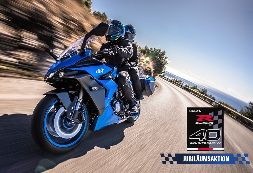 Eine blaue GSX-S1000GT mit zwei Personen auf einer kurvigen Landstraße, rechts unten mit Jubiläumsaktions-Logo