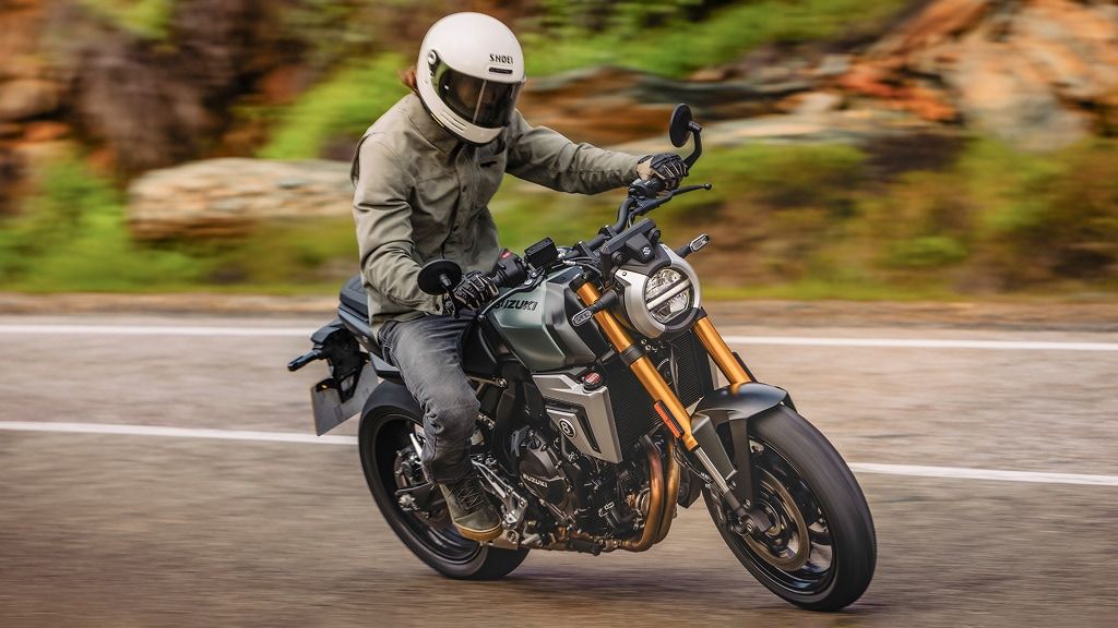 Motorradfahrer mit weißem Helm und beiger Jacke fährt eine Suzuki GSX-8T dynamisch durch eine Kurve auf einer Landstraße
