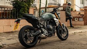 Suzuki GSX-8T in grün-schwarzer Lackierung steht am Straßenrand vor einem Wohnhaus, im Hintergrund steht eine Person mit Motorradhelm