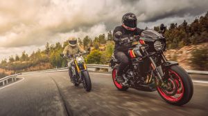 Zwei Motorradfahrer fahren sportlich durch eine kurvenreiche Landstraße, vorne eine schwarze Suzuki GSX-8TT mit roten Felgen, dahinter eine Suzuki GSX-8T, bei bewölktem Himmel