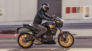 Motorradfahrer mit schwarzer Lederjacke und Helm fährt eine grüne Suzuki GSX-8TT mit goldenen Felgen durch die Stadt.