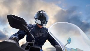Nahaufnahme eines Motorradfahrers mit dunklem Helm und Motorradjacke, aufgenommen aus einer tiefen Perspektive mit Wolkenhimmel im Hintergrund.
