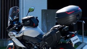 Ein weißes Suzuki-Motorrad mit montierten Touring-Koffern und Topcase steht vor einem Gebäude; Fokus auf Gepäcksystem und Rückansicht des Motorrads.