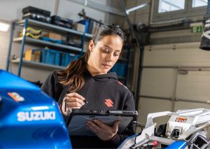 Eine Mechanikerin nutzt ein Tablet zur Diagnose oder Reparatur eines Motorrads in einer Werkstatt.