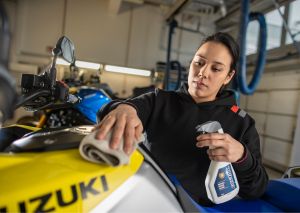Eine Mechanikerin reinigt den Tank eines Suzuki-Motorrads mit einem Reinigungsspray