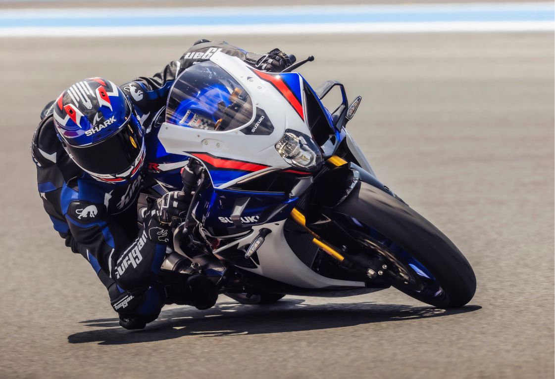 Fahrer in Rennmontur legt sich mit der neuen Suzuki GSX-R1000R 40th Anniversary Edition in weiß-blauer Sonderlackierung und Jubiläums-Emblem tief in die Kurve auf einer Rennstrecke