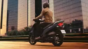 Fahrer auf Suzuki Scooter in der Stadt, Heckansicht bei Dämmerung vor Hochhäusern in Fahrt.