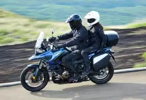 Paar fährt auf blauer Suzuki V-Strom 1050 mit Koffersystem auf einer kurvigen Straße.