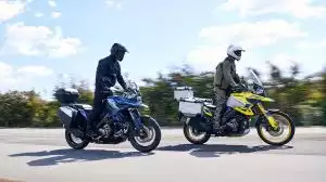 Zwei Suzuki Adventure-Bikes mit Alukoffern auf Landstraße, Fahrer im Touring-Outfit.