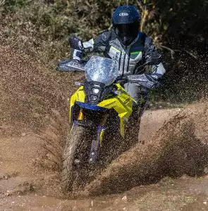 Gelbes Suzuki-Motorrad fährt durch schlammiges Gelände, Fahrer in Schutzkleidung.