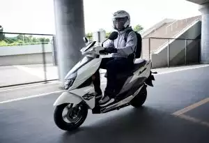 Fahrer auf weißem Suzuki Avenis Roller unter Brücke
