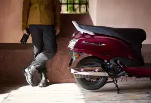 Roter Suzuki Address 125 Roller rechts geparkt neben einer Person in Motorradkleidung.