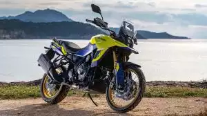 Suzuki V-Strom 800DE in Gelb als Reiseenduro am Küstenufer mit Meer und Bergen im Hintergrund