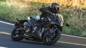 Sportlicher Fahrer auf schwarzer Suzuki meistert eine Kurve auf sonniger Landstraße.