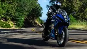 Blaues Suzuki GSX-8r Sportmotorrad fährt dynamisch durch eine Kurve auf bewaldeter Straße.