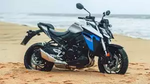 Eine silbern-blaue Suzuki GSX-S950 als Naked Bike, geparkt auf einem Sandstrand, mit dem Meer im Hintergrund.