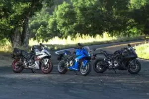 Drei Suzuki Motorräder auf einer kurvigen Landstraße im Grünen.