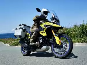 Suzuki V-Strom 1050DE mit Alukoffern an Küstenstraße, Fahrer in Fahrt vor Meerblick.