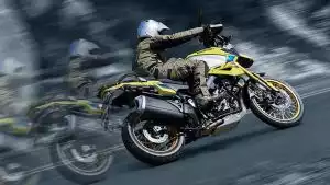 Ein Fahrer auf einer gelben Suzuki V-Strom 1050DE in Schutzkleidung und Helm fährt dynamisch auf einer kurvigen Straße.