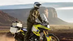 Ein Motorradfahrer in Schutzkleidung auf gelber Suzuki V-Strom 1050DE mit Koffern vor einer felsigen Wüstenlandschaft.