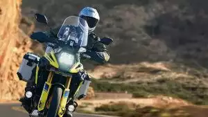 Motorradfahrer mit silbernem Helm auf gelber Suzuki V-Strom 1050DE auf einer Straße in einer Wüstenlandschaft.