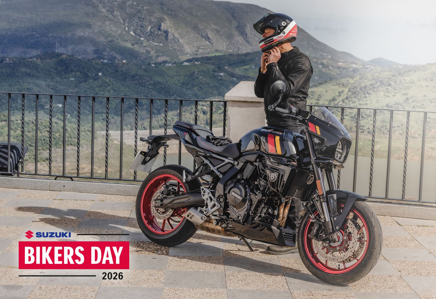 Suzuki GSX-8TT im Café-Racer-Design mit roten Felgen vor Bergpanorama, daneben ein Fahrer in Lederjacke. Im Bild der Hinweis auf den Suzuki Bikers Day 2026.