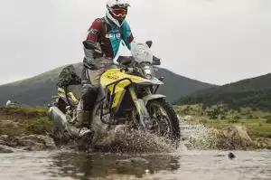 Motorradfahrer auf Suzuki Adventure-Bike überquert Fluss in bergiger Landschaft