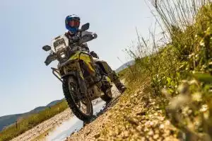 Motorradfahrer auf Suzuki Adventure-Bike auf Schotterweg in sonniger Landschaft