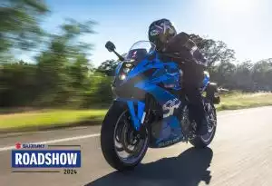 Fahrer auf blauer Suzuki GSX-8R fährt Landstraße entlang, bewirbt Suzuki Roadshow 2024 Event.