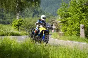 Motorradfahrer auf Suzuki-Motorrad in grüner Landschaft auf kurviger Straße