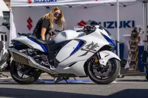 Frau betrachtet Suzuki-Motorrad auf einem Motoradfestival, im Hintergrund Suzuki-Logo.
