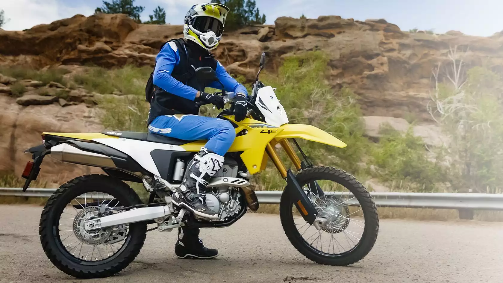 Gelbe Suzuki DR-Z400 Enduro mit Fahrer in voller Montur, bereit für Offroad-Abenteuer in felsiger Landschaft.