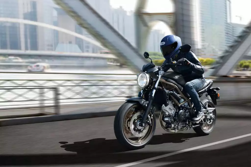 Fahrer auf dunkelgrauer Suzuki SV650 fährt dynamisch über eine Brücke mit moderner Stadtkulisse.