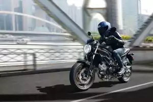 Fahrer auf dunkelgrauer Suzuki SV650 fährt dynamisch über eine Brücke mit moderner Stadtkulisse.
