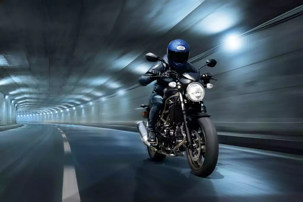Fahrer auf dunkelgrauer Suzuki SV650 Naked Bike fährt dynamisch durch einen hell beleuchteten Tunnel.