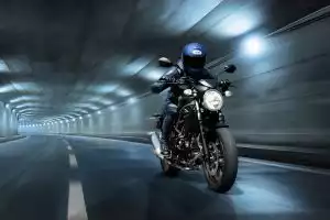 Fahrer auf dunkelgrauer Suzuki SV650 Naked Bike fährt dynamisch durch einen hell beleuchteten Tunnel.