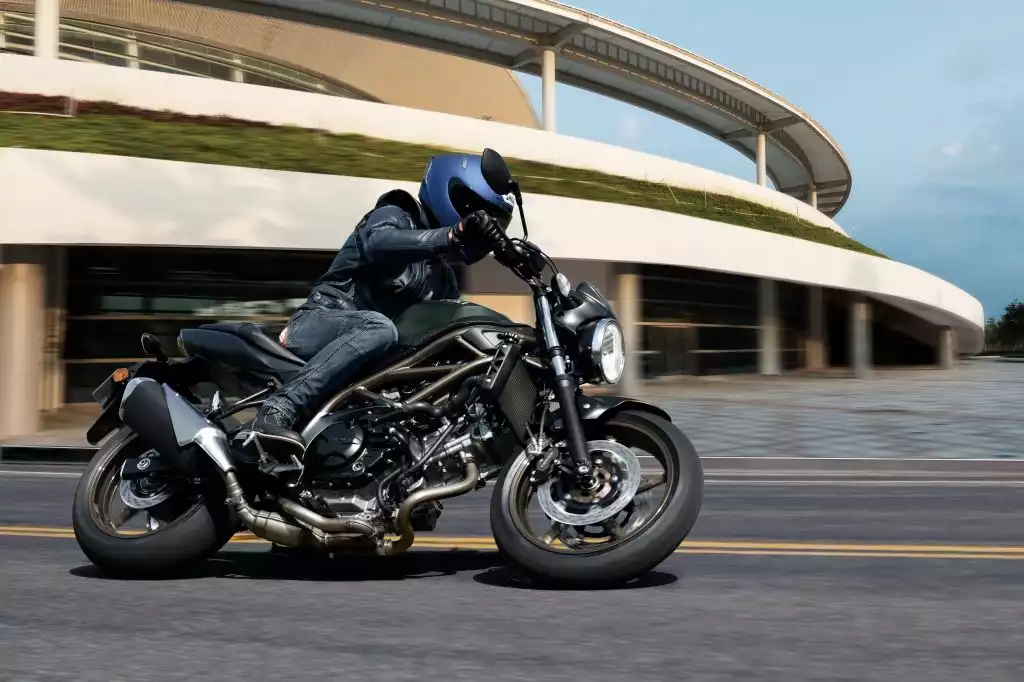 Fahrer auf Suzuki SV650 fährt dynamisch in Kurve vor moderner futuristischer Architektur.