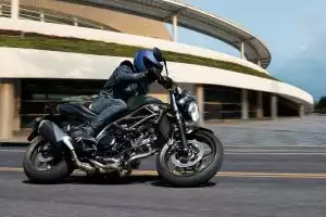 Fahrer auf Suzuki SV650 fährt dynamisch in Kurve vor moderner futuristischer Architektur.