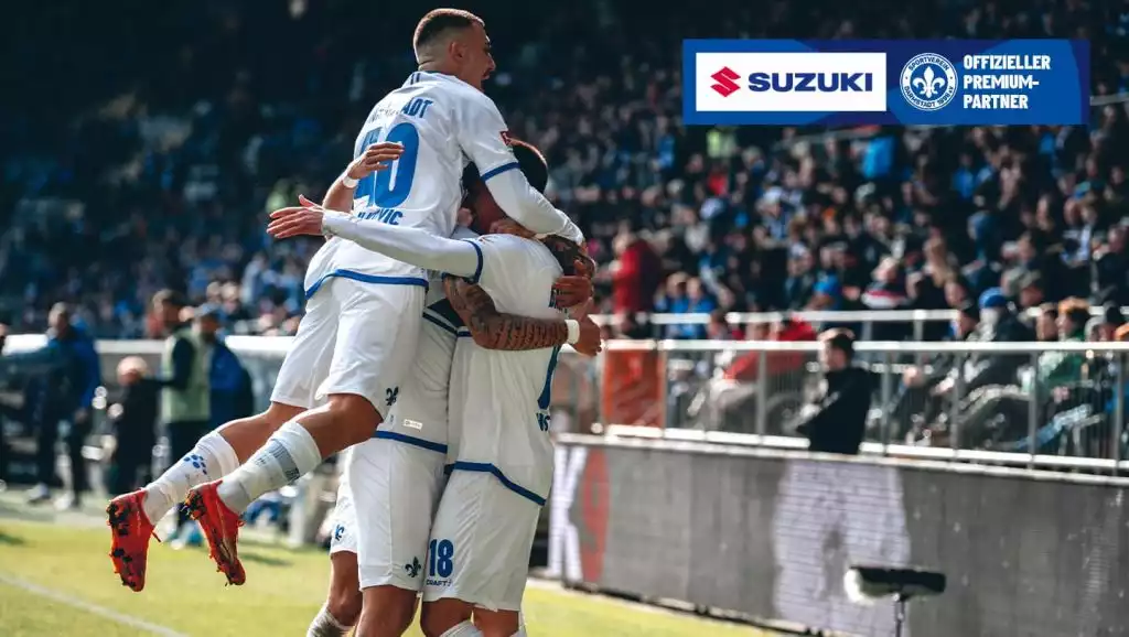 Fußballspieler jubeln auf dem Spielfeld, Suzuki-Logo als offizieller Premium-Partner im Hintergrund