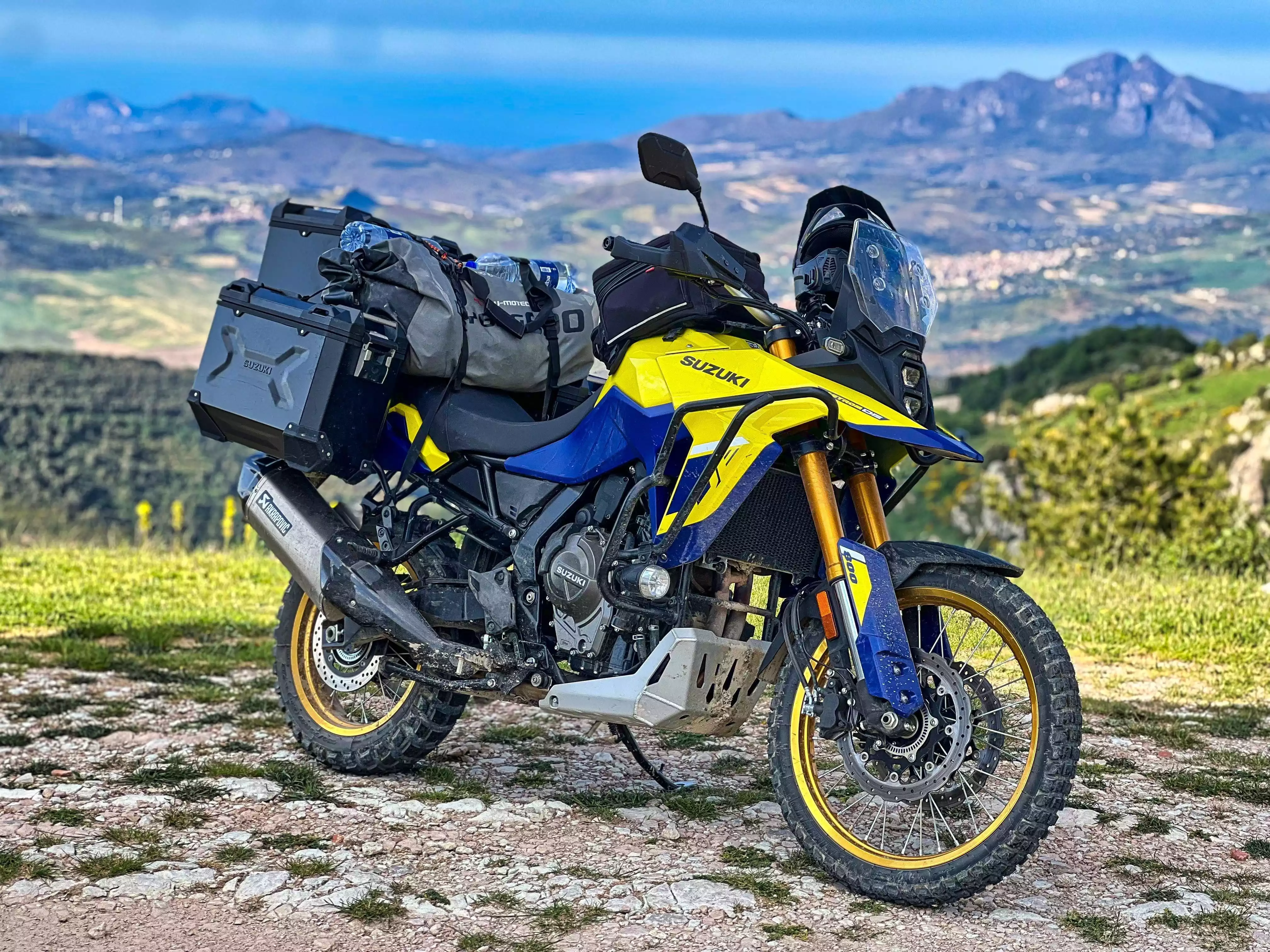 Gelbes Suzuki Adventure-Motorrad mit Gepäckträger vor Berglandschaft.