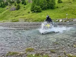 Motorradfahrer überquert spritzend einen Gebirgsbach auf Suzuki-Motorrad.