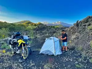 Motorradfahrer beim Camping neben Suzuki Adventure-Bike in bergiger Landschaft