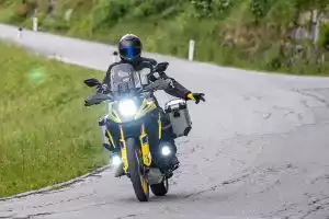 Motorradfahrer auf Suzuki V-Strom 1050 mit Zusatzleuchten auf kurviger Straße, Fokus auf Sichtbarkeit und Sicherheit.