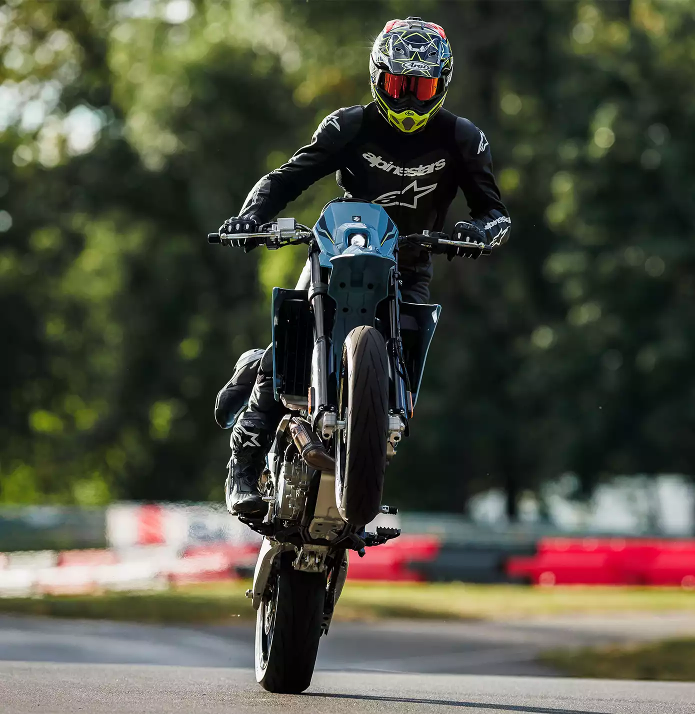 Fahrer auf Suzuki DR-Z4SM Motorrad in schwarzer Schutzkleidung bei Wheelie auf Rennstrecke