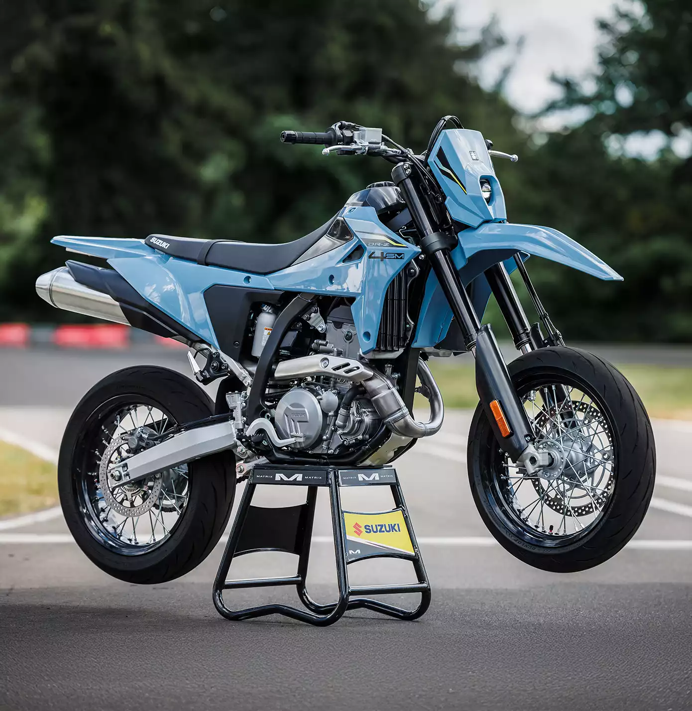 Blaues Suzuki DR-Z4SM Motorrad auf Ständer, seitliche Ansicht auf Rennstrecke