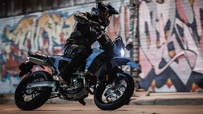 Motorradfahrer auf blauer Suzuki Supermoto in Kurvenfahrt, vor farbenfrohen Graffiti-Wänden in urbaner Umgebung.