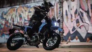 Motorradfahrer auf blauer Suzuki Supermoto in Kurvenfahrt, vor farbenfrohen Graffiti-Wänden in urbaner Umgebung.