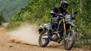 Motorradfahrer auf Suzuki DR-Z4S fährt dynamisch auf Schotterweg durch grüne Landschaft.