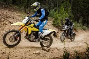 Zwei Fahrer auf Suzuki DR-Z4S Motorrädern in gelb und schwarz auf einer Offroad-Strecke im Wald