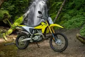 Gelbe Suzuki DR-Z400S Enduro-Motorrad steht geparkt vor einem imposanten Wasserfall im Wald, bereit für Abenteuer.